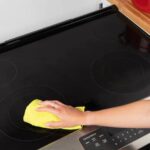 A person cleaning a glass top range with a microfiber cloth and cleaner.