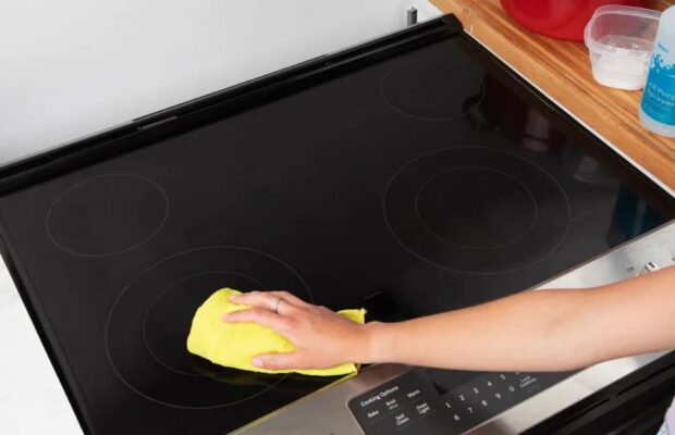A person cleaning a glass top range with a microfiber cloth and cleaner.